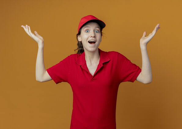 年轻令人印象深刻的年轻漂亮的送货女孩在红色制服和帽子显示空手孤立在橙色的背景女孩印象背景