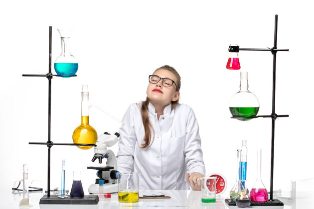 烧杯前视图穿着白色医疗服的女医生正坐在桌子前 解决白色背景病毒的化学大流行医生医学化学