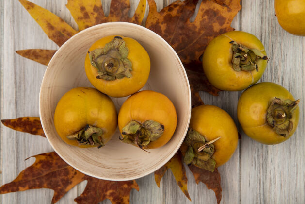 视野新鲜柿子水果的顶视图在一个碗上 叶子放在一张灰色的木桌上木头灰色柿子