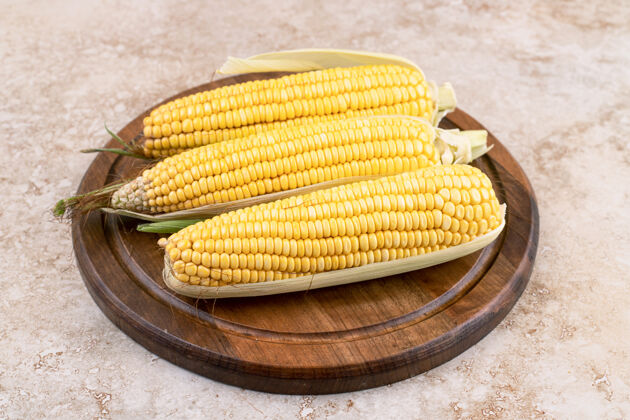 食物三个生玉米放在大理石表面的木板上玉米黄色玉米