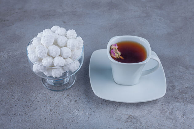 甜点一碗白甜甜的糖果和一杯茶放在石头表面花蕾杯子茶碟