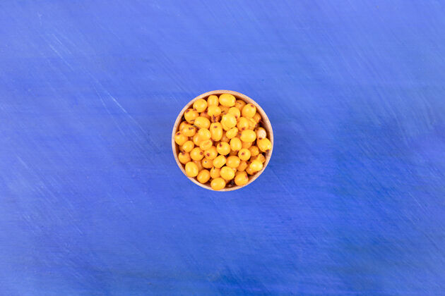 食物蓝色表面上盛满黄樱桃的小木碗黄色红色堆
