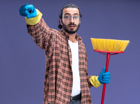 帅哥年轻帅气的清洁工穿着t恤 戴着手套 拿着拖把 在蓝色的墙上展示着你们被隔离的姿势穿印象年轻