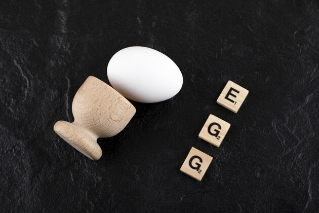 家禽一个鸡蛋和一个木制字母 在黑色的表面上拼写为鸡蛋农业膳食生的