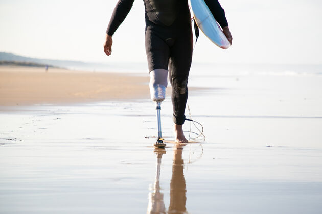 强壮无法辨认的冲浪者用假腿在海边行走度假穿着运动员