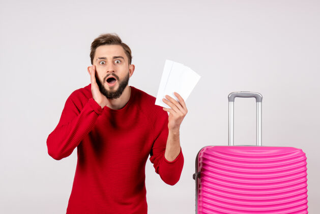 成人正面图：年轻男性 带着粉色包 手持机票 在白墙上航行 彩色旅行 旅游度假照片微笑航班年轻男性