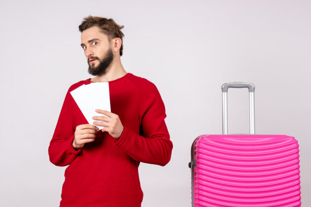 成年人正面图：年轻男性 带着粉色包 手持白墙旅行票 彩色度假航班 夏季旅游者年轻男性微笑航班