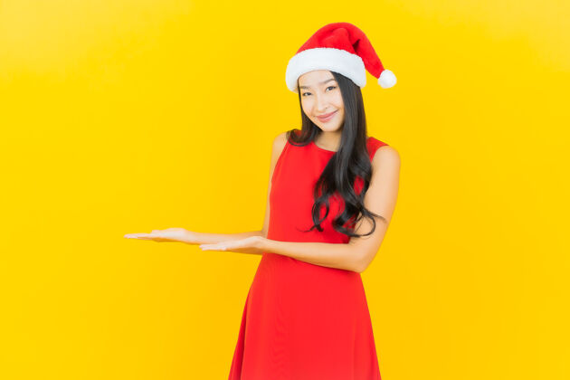 积极肖像美丽的亚洲年轻女子戴圣诞帽或发带在黄色的墙上圣诞老人表情女性