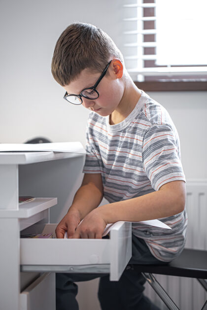 作业戴眼镜的小男孩坐在笔记本电脑前的桌子旁 在抽屉里找东西孩子眼镜抽屉