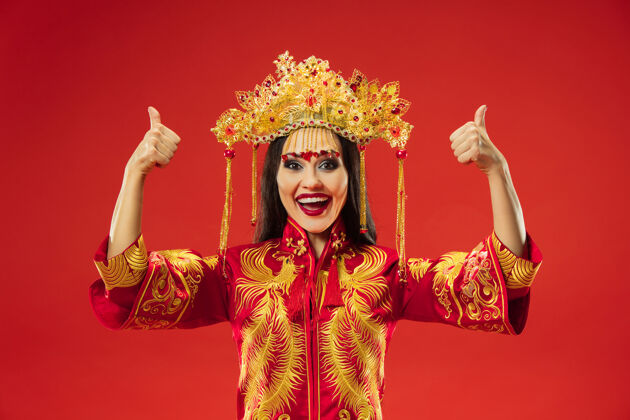 新中国传统的优雅女子在摄影棚的红色背景美丽的女孩穿着民族服装中国新年 优雅 优雅 表演者 表演 舞蹈 女演员 情感概念肖像中国人文化