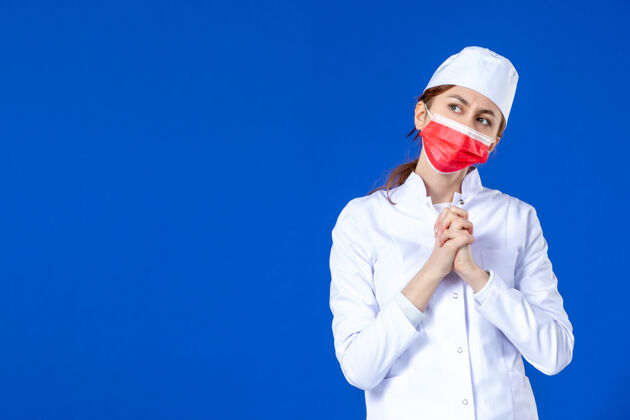 疾病正面图蓝色墙上戴着红色面罩的年轻护士 穿着医疗服药品医院套装