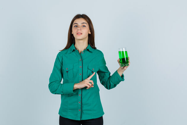 衬衫年轻女孩穿着绿色上衣 黑色裤子 手里拿着一杯绿色液体 用食指指着它 目光集中 俯视前方女孩年轻拿着