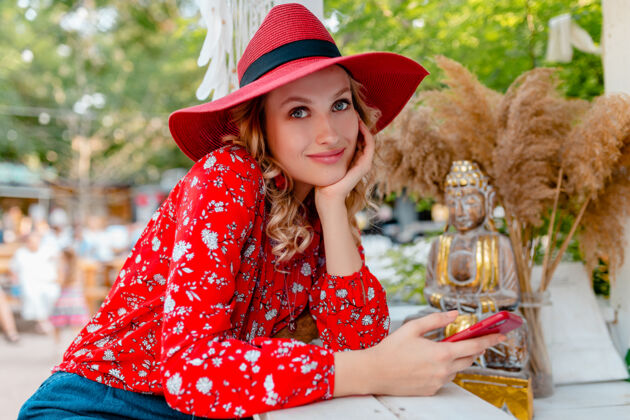 情感迷人的时尚金发微笑的女人在稻草红帽子和衬衫夏季时尚服装举行使用智能手机咖啡厅服装帽子手机