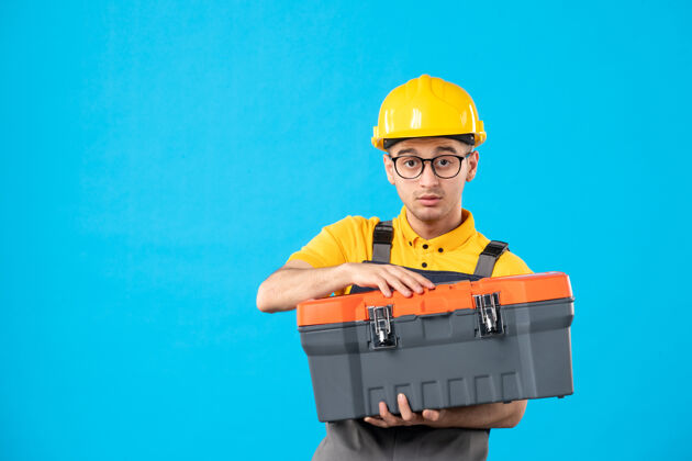 工人蓝色表面上穿着制服的男建筑工人手拿工具箱的正面图视图手工具