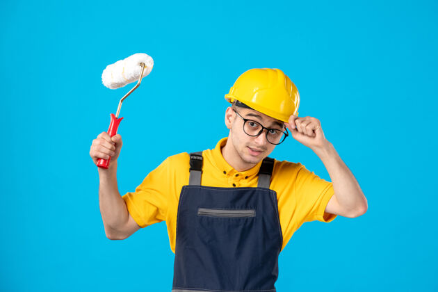 蓝前视图中的男性建筑工人制服与油漆辊在他手中的蓝色表面承包商工作工人