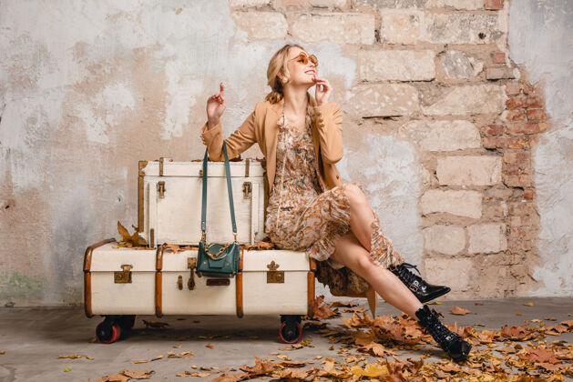 外套在街上 穿着米色外套的金发美女坐在手提箱上对着墙季节包美丽