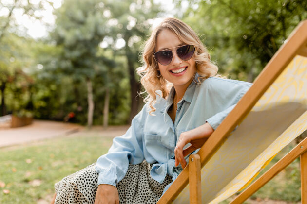衣服迷人的金发微笑的女人坐在躺椅上穿着夏天的衣服快乐休闲穿