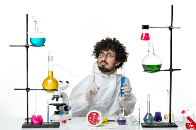实验正面图：年轻的男科学家穿着特制的衣服 拿着装有溶液的烧瓶 挂在浅白的墙上实验室玻璃容器