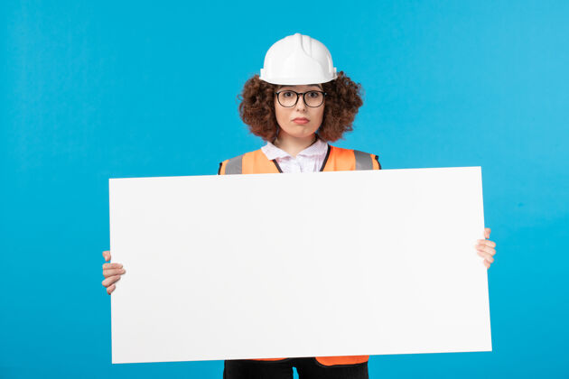 女性身着制服的女建筑工人正拿着蓝色墙壁上的普通办公桌工作建筑商背心