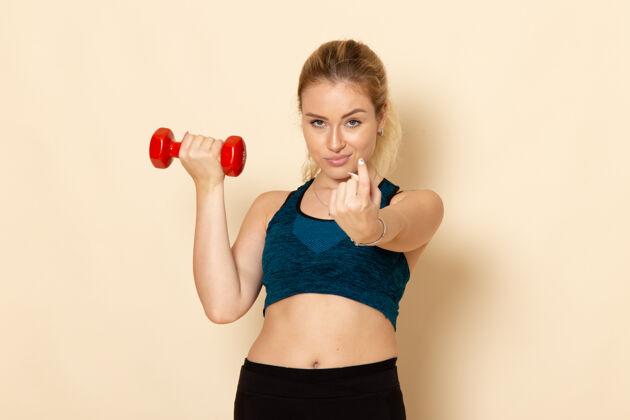 体重正面图身穿运动装的年轻女性手持红色哑铃在白墙上健康运动美体锻炼年轻女性运动器材健身