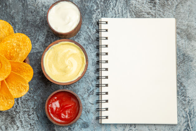 蛋黄酱自制的薯片装饰像花形和盐番茄酱蛋黄酱和笔记本放在灰色的桌子上碗封闭蜡封