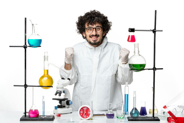 套装正面图身着白色特制西服的年轻男科学家站在桌子旁 拿着解决方案欢呼雀跃特别实验室欢呼