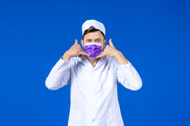 电话前视图中的男医生穿着医疗服和紫色面具显示电话呼叫poseon蓝色表演医院疫苗