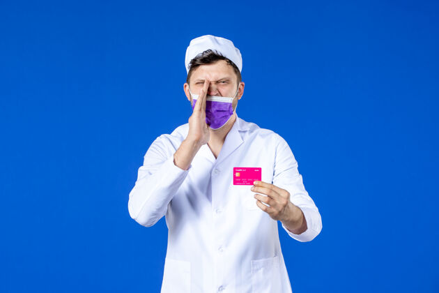 实验室外套前视图中的男医生穿着医疗服和紫色面具持有信用卡在蓝色诉讼医学病毒
