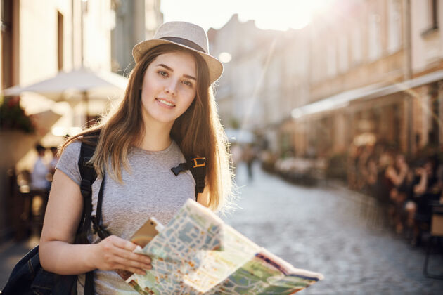 地图一个女人用地图和平板电脑环游世界 站在欧洲的一个小城市里看着相机的肖像目的地街道背包