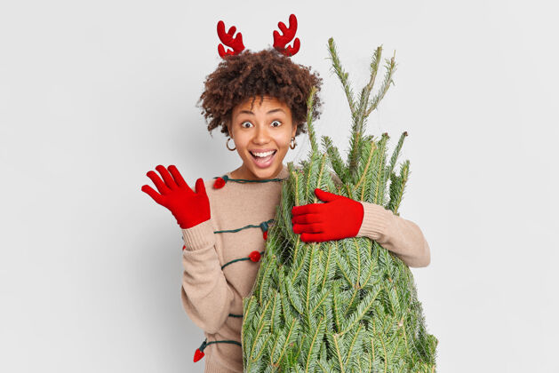 驯鹿节日购物理念积极向上的民族妇女穿着红驯鹿鹿角和手套 挥手致意 在街市上选择圣诞树 在家里装饰新年快乐背心快乐你好