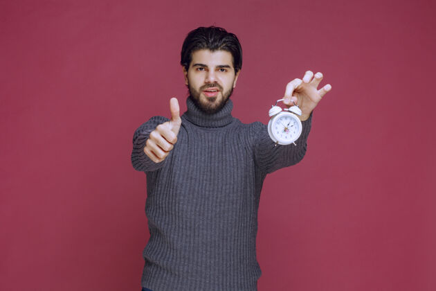 年轻人一个男人拿着一个白色闹钟 指着一个最好的报价产品休闲人体模型