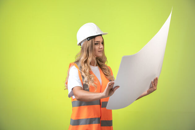 背景戴着白色头盔和装备的女工程师正在检查施工图并阅读企业薪资制造