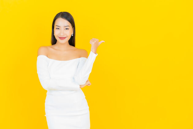 正式在黄色的墙上 一位年轻漂亮的亚洲商业女性微笑着指着旁边的白色西装时尚肖像人