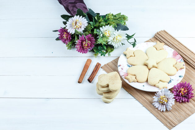 堆叠高角度观看心形和星型饼干 鲜花放在肉桂垫上饼干烘焙巧克力