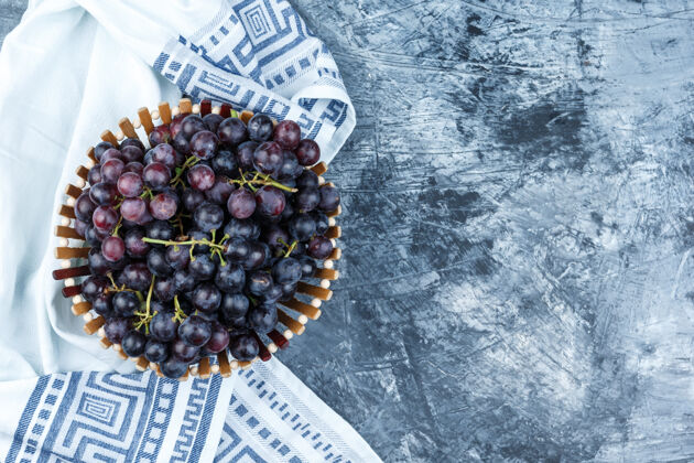 树叶黑葡萄在一个篮子里平放在肮脏的石膏和厨房毛巾背景秋天厨房成熟