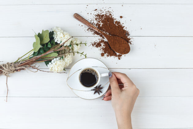 一套磨碎的咖啡 鲜花 香料和女性手拿着一杯咖啡的木制背景平放杯子豆类摩卡咖啡