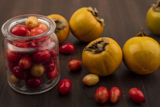玻璃玻璃罐上红色的科尼莉亚樱桃的顶视图 柿子水果被隔离在木制表面上美味营养食品