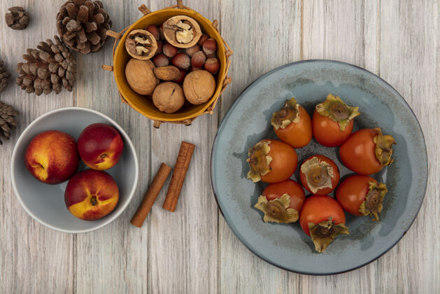 饮食桃子放在碗里 柿子放在盘子里 桂皮条和坚果放在灰色木质表面的桶上柿子营养农业