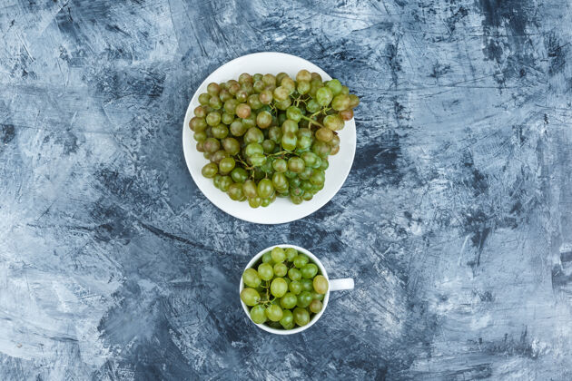 秋天顶视图绿色葡萄在白色的盘子和杯子上 背景是灰泥水平夏天水果石膏