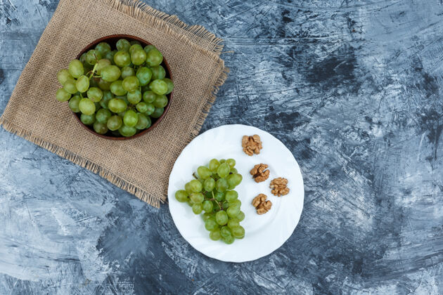 叶子平躺在碗里的白葡萄与葡萄 核桃在一个白色的盘子上深蓝色大理石背景水平自然水平盘子