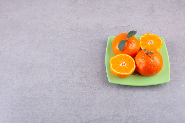 健康整个橘子和切成片的橘子放在绿色的盘子里新鲜热带克莱门汀