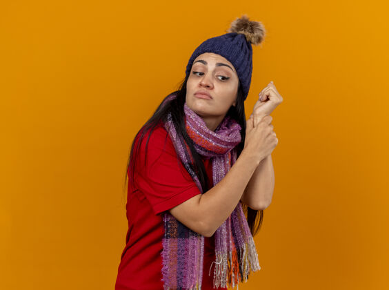 帽子集中年轻的白种人生病的女孩戴着冬天的帽子和围巾检查脉搏看边隔离在橙色的墙壁与复制空间检查疾病年轻