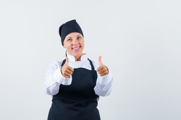 快乐身着制服的女厨师 围裙上竖起大拇指 看上去很欢快 正面视图可爱美女肖像