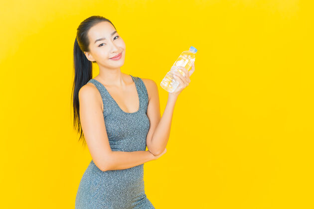 亚洲在黄色的墙上画一幅美丽的亚洲年轻女子 穿着运动服 喝着瓶装水漂亮护理运动