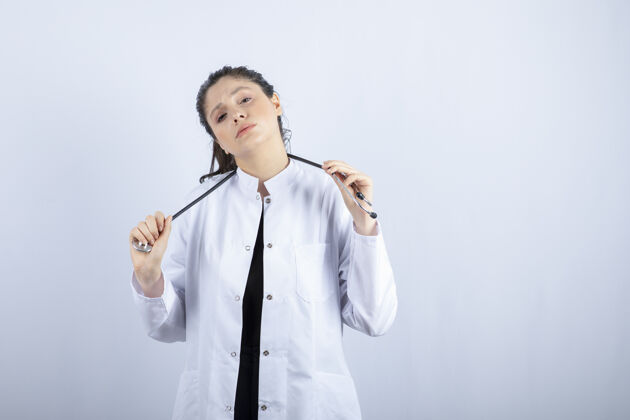 女人穿着白大褂的漂亮女医生在白墙上摆好听诊器的姿势医生工人自信
