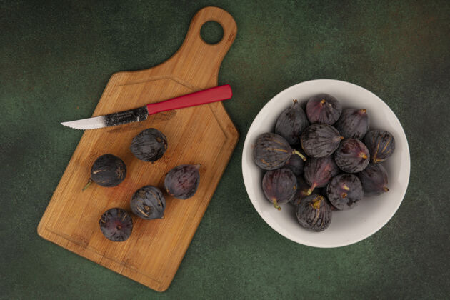 新鲜甜甜的黑色任务无花果的顶视图与黑色无花果在一个木制的厨房板上与刀子在绿色的墙上食物木材刀