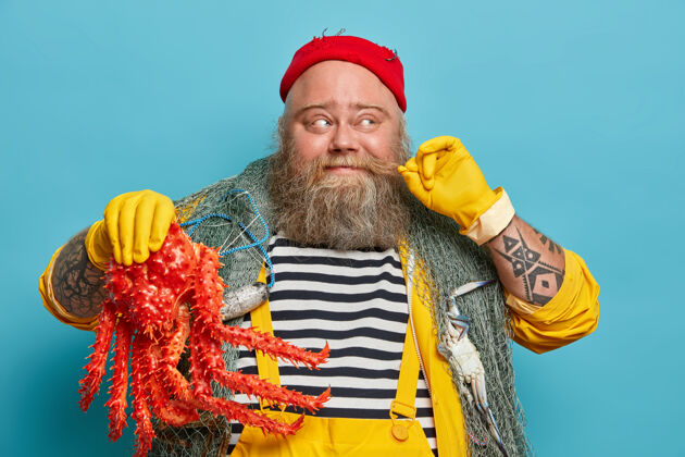 卷发开朗的水手卷起小胡子 抱着大海洋生物 穿着条纹套头衫和黄色工作服人类螃蟹男