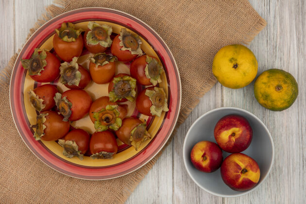 盘子新鲜柿子放在布袋上的盘子上 桃子放在碗里 橘子被隔离在灰色的木墙上水果秋天风景