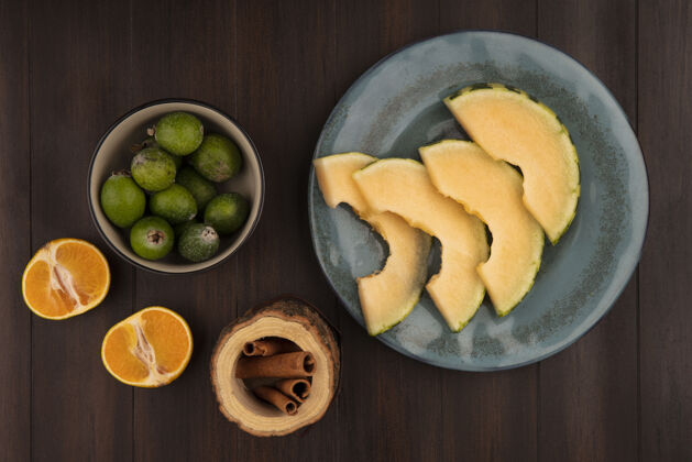 水果一个盘子上的哈密瓜片的俯视图 碗上的蜜饯 木墙上的桂枝和橘子顶部哈密瓜饮食