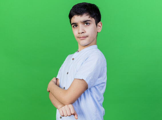 男孩自信的小男孩站在封闭的姿态在侧视图看前面的绿色隔离墙衣服姿势封闭